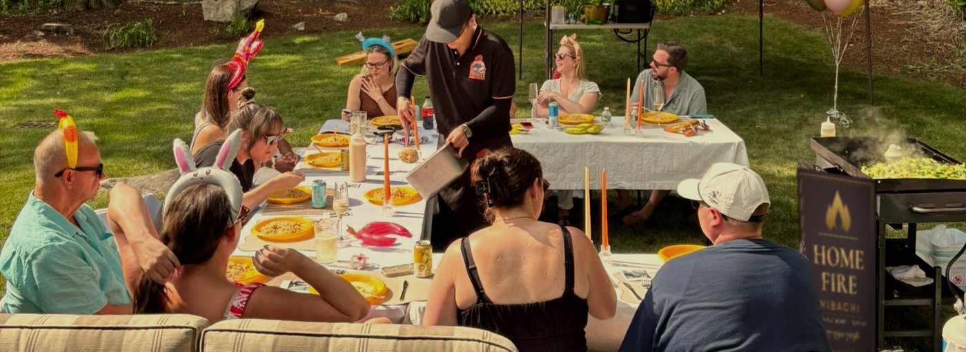Hibachi chef serving a birthday party at long tables on a backyard lawn