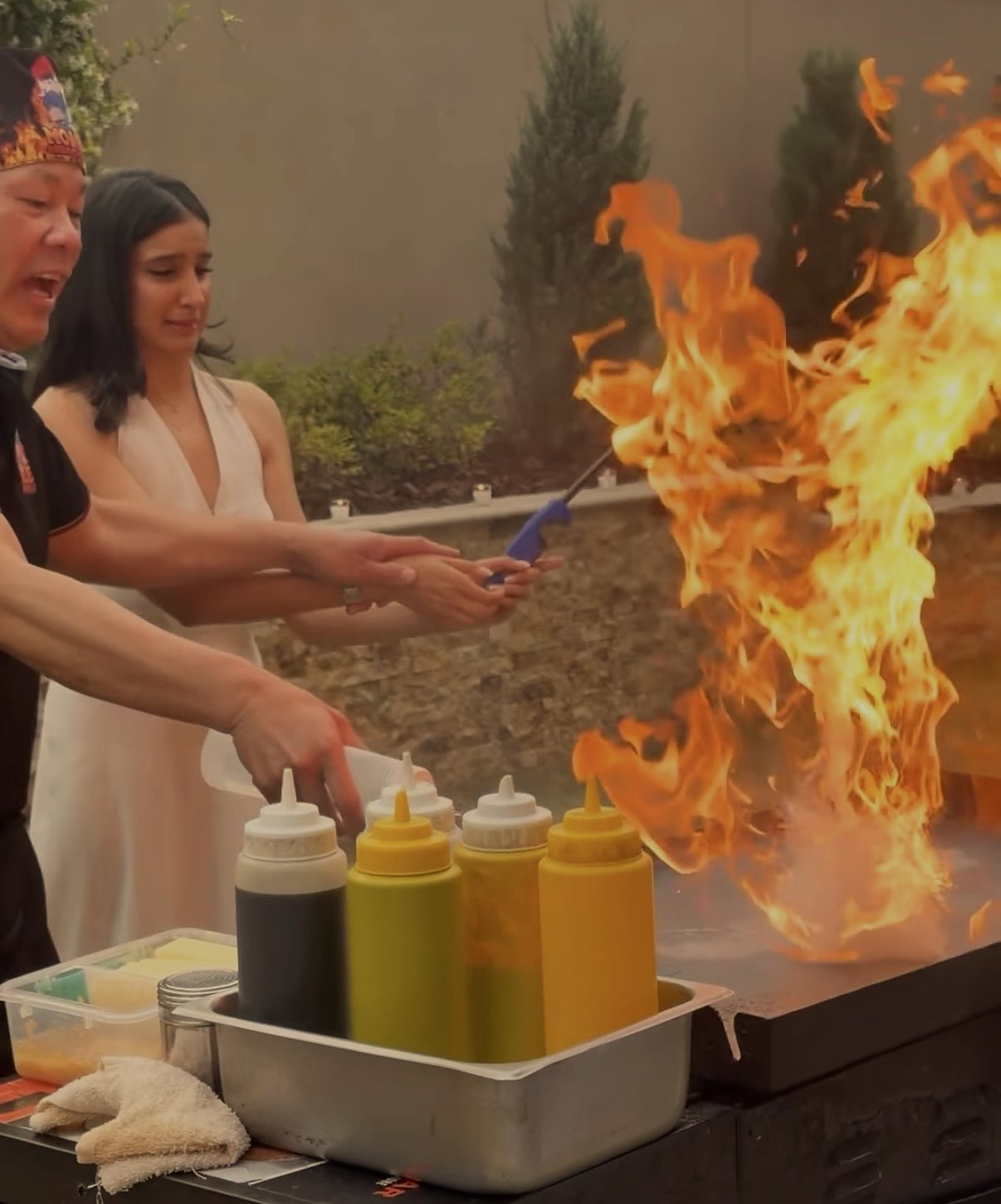 Hibachi chef and a guest lighting a tall grill flame at a backyard hibachi party